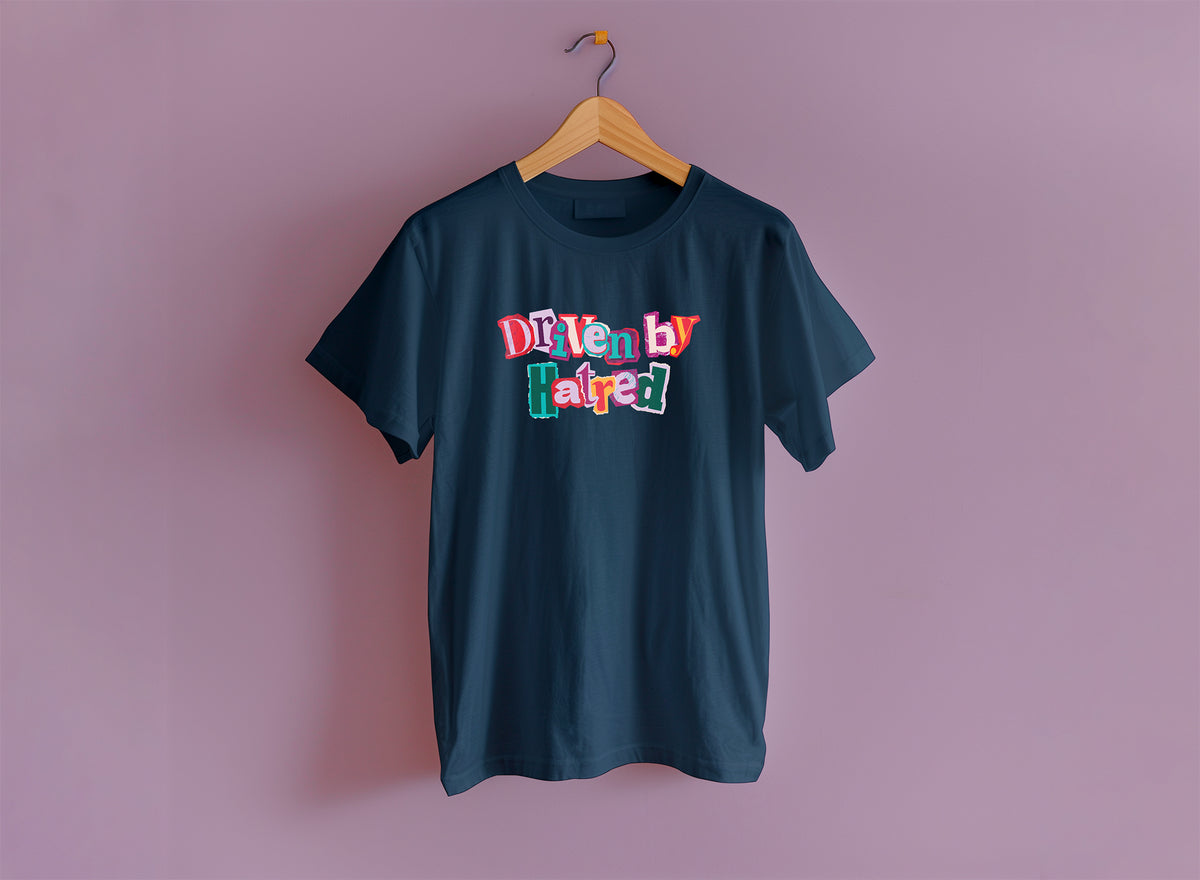 A navy short sleeve t-shirt hangs from a wooden hanger on a lavender purple backdrop. The shirt says "driven by hatred" in a colorful cut out collage style.