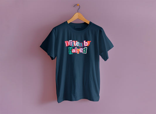 A navy short sleeve t-shirt hangs from a wooden hanger on a lavender purple backdrop. The shirt says "driven by hatred" in a colorful cut out collage style.